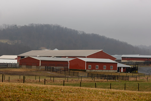 Red barn and outbuilding sit on fenced in pastures next to a hill in rural Virginia, USA