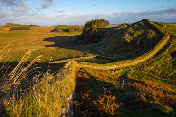 Full shot of mother and son walking alongside Hadrian's Wall, Northumbria. They are wearing casual sports clothing on a summer's day and engaging in conversation.
