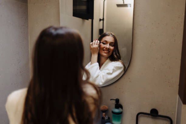 istock Young woman putting mascara, while observing herself in the mirror 2135719217