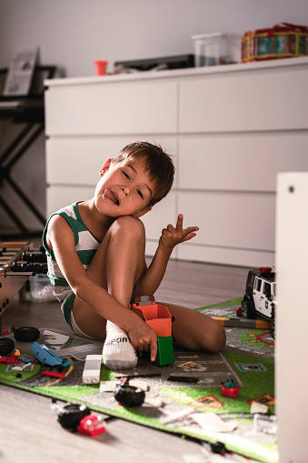 Joyful boy making silly faces, engaged in play with his toys, in a sunlit modern room.