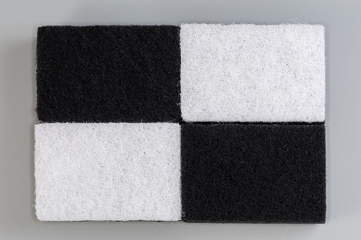 Several black and white kitchen soft synthetic cleaning sponges laid out hard urethane abrasive layer up on a gray background, top view