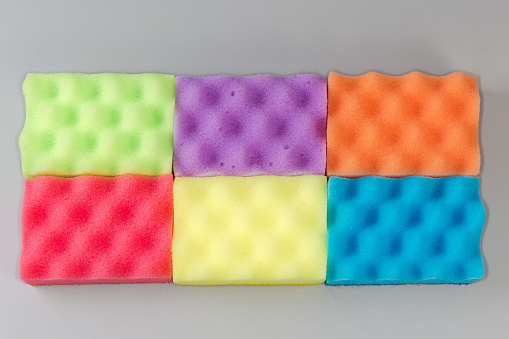 Several multi colored kitchen soft synthetic cleaning sponges laid out on a gray surface