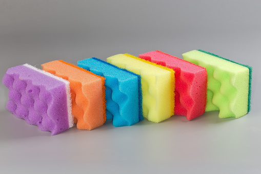 Several multi colored kitchen soft synthetic cleaning sponges with hard urethane abrasive layer on a gray background