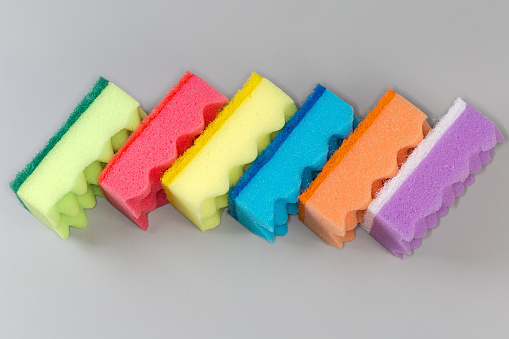 Several multi colored kitchen soft synthetic cleaning sponges with hard urethane abrasive layer laid out on a gray surface