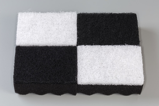 Several black and white kitchen soft synthetic cleaning sponges laid out hard urethane abrasive layer up on a gray background