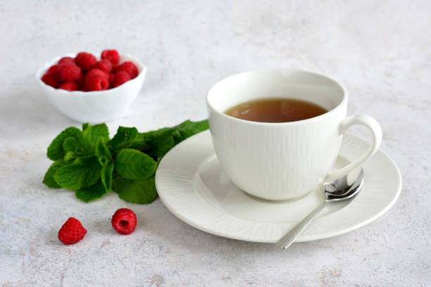 istock a cup of tea and a spoon on a saucer with mint and raspberry 2135735270