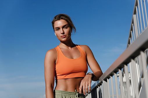 Young Woman Fitness Enthusiast Wearing an Orange Sports Bra Resting Outdoors.
