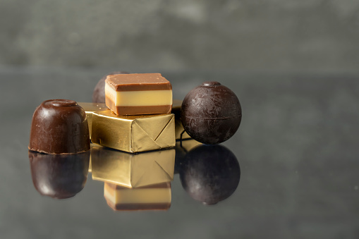 Several chocolates, including an open cube, arranged on a dark surface where the chocolates are reflected. High quality photo