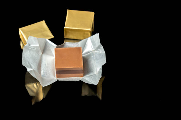 A single chocolate cube sits unwrapped among closed chocolates against a black background. High quality photo
