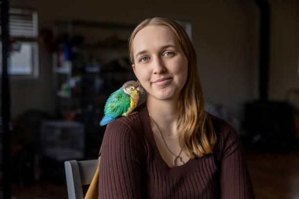 Portrait of a young woman at home with her green-cheek Conure named Momo.