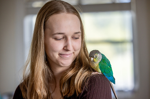 Portrait of a young woman at home with her green-cheek Conure named Momo.