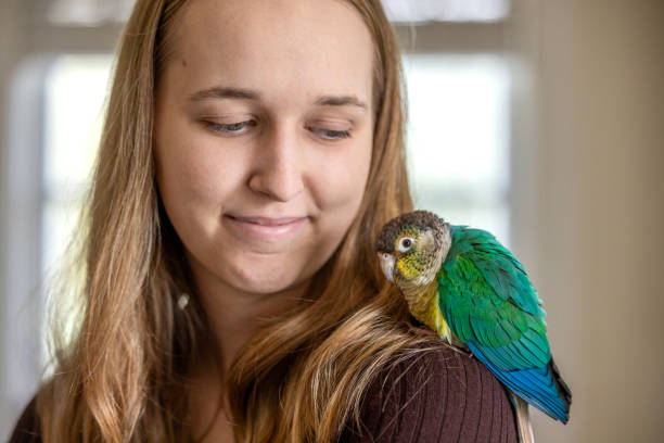 Portrait of a young woman at home with her green-cheek Conure named Momo.