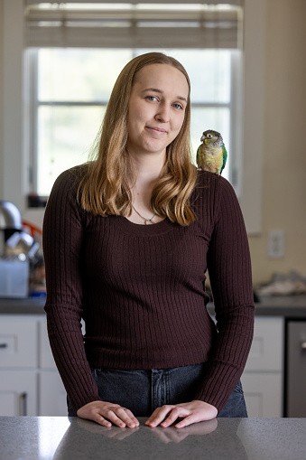Portrait of a young woman at home with her green-cheek Conure named Momo.