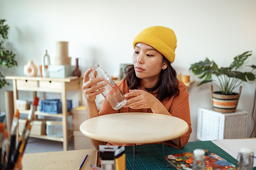 Hipster female artist working at her home based workshop, holding glass bottle