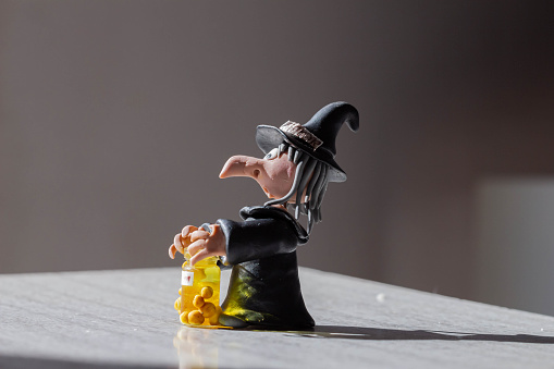 Witch figurine with bottle of potion and candle on the table.Candle holder with the figure of a witch on a mirror background