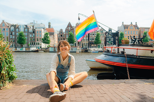 Portrait of  woman sitting on the background of LGBTQ+ flag on the boat in Amsterdam