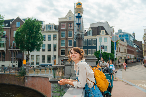 Cheerful woman standing on the bridge overlooking canal while walking in Amsterdam in summer
