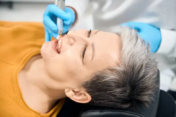 Male dentist meticulously removing plaque and tartar buildup during professional hygienic teeth cleaning to adult woman patient, ensuring the client's oral health