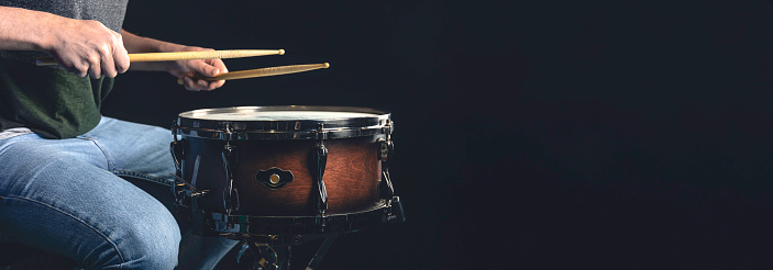 A man plays a snare drum on a dark background, copy space. Web, social media banner template.