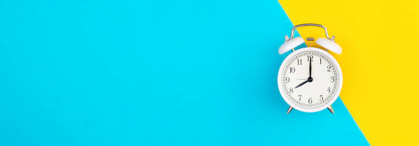 istock White alarm clock on a blue and yellow background, flat lay. 2135837539