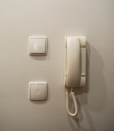 Intercom handset and two white light switches on a white wall.