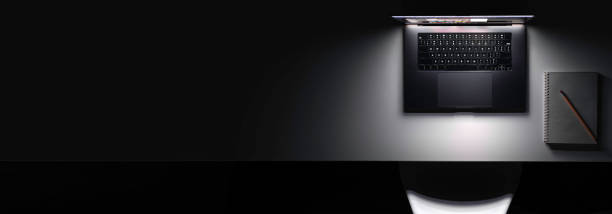 Laptop with a glowing screen on a table in the dark, top view, copy space.