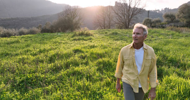 Mature man walks across lush field at sunset
