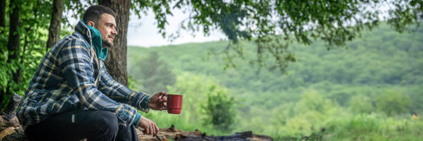 istock A man with a cup of warming drink warms himself by the fire in the forest. 2135890113