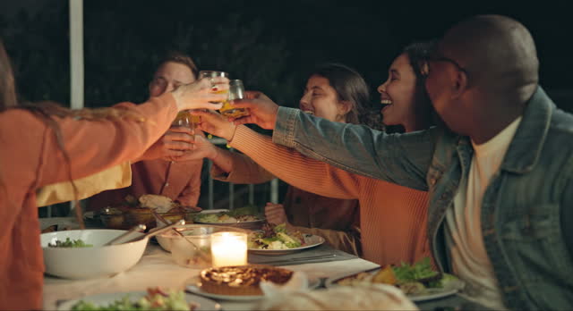 Friends, group toast and dinner on patio, night and conversation with food, new years eve and party. Women, man and outdoor at table with juice, memory or celebration with cheers, diversity or goals