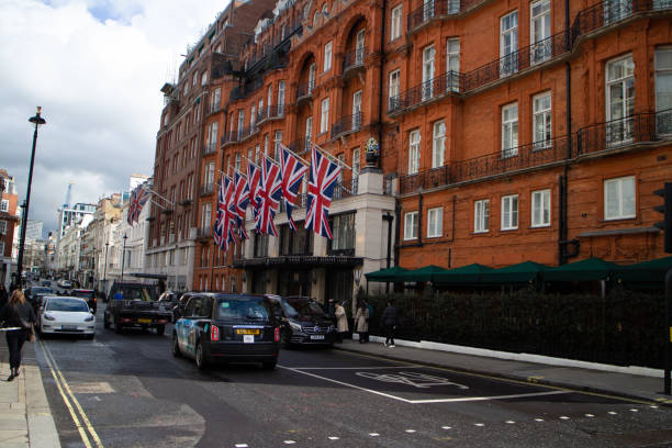 5 star hotel on Brook Street in London. The building has a row of Union Jack flags as decoration on the front above the door and an iconic London Taxi in the middle of the road