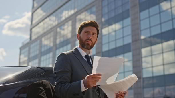 Thoughtful director reading contract at sunny business area. Boss looking deal Thoughtful director reading contract at sunny business area zoom out. Serious bearded businessman looking on deal terms standing street. Elegant middle-aged boss examining work documents near auto. city zoom out stock pictures, royalty-free photos & images