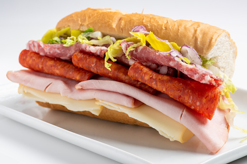Sliced ham, Pepperonni, salami,  Cheese, lettuce, Pepperoncini peppers  and onion submarine sandwich on white background