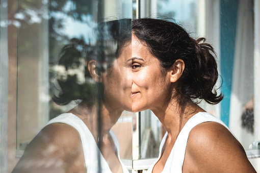 mid adult woman looking out of window and reflecting in pane