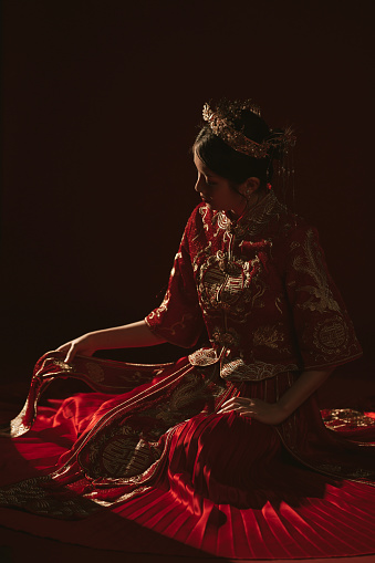 Backlit portrait of an Asian Chinese woman in traditional bridal tea dress and headwear kneeling on the floor