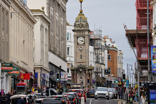 Brighton, Brighton And Hove, East Sussex, Southeastern England, United Kingdom, Britain, Europe - 16th March 2024: West Street, the most exclusive part of the town and the Jubilee Clock Tower (built in 1888) and some people are walking along the footpath, enjoying leisure activities and embracing an active lifestyle. A Listed Building – Grade II.\n\nThese houses were built there (along West Street) in the late 18th and early 19th centuries.