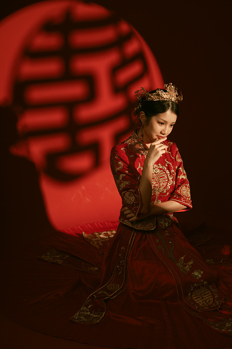 Beautiful Asian Chinese in traditional Chinese bridal tea dress kneeling before a gobo lighting effect that spells “bliss” in Mandarin
