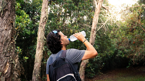 tired hiker resting and drinking water from a plastic bottle in the mountain at morning