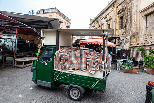 Palermo, Italy - May 13, 2023: Piaggio tricycle parked in Ballaro Market, street food market with people around in Palermo, Sicily, Italy