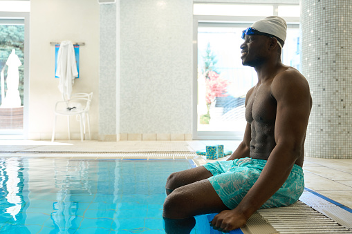 Side view of joyful sportsman sitting on edge of indoor swimming pool