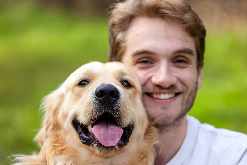 Portrait of happy young man sitting in the park with his pet Golden Retriever, front view, background with copy space, full frame horizontal composition
