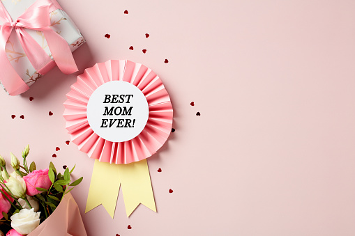 Best mom ever rosette, gift box, bouquet of flowers, confetti on pastel pink background. Top view. Flay lay