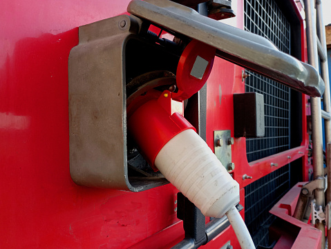 Charging electric batteries of a big red truck from the mains. The electric cable is inserted into the car socket.