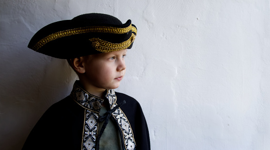 Little boy dressed in Rococo era costume in a black coat and black hat on a white background