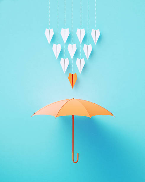 istock Paper Planes Flying Towards A Coral Colored Umbrella On Blue Background 2136187325
