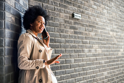 Young cheerful black woman talking on the phone in front of a brick wall