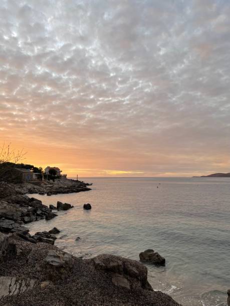 Sunset casting a warm afterglow over lake with rocky shore, under a cloudy sky