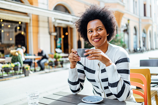 Young cheerful black woman enjoys a cup of coffee at a sidewalk café