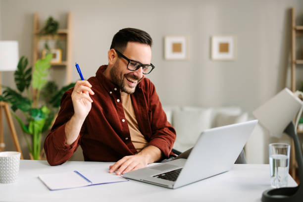 istock Satisfied young man working at home with laptop and papers on desk 2136274853