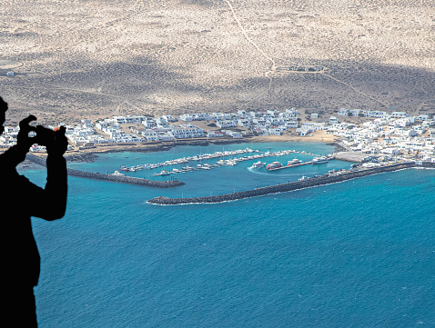 Silhouette of a man taking a photograph of an island from a high vantage point - beautiful sea and landscape and spectacular views.