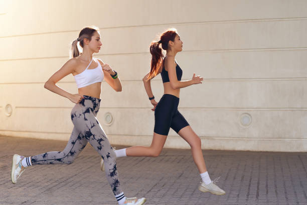 istock Two active women athlete running on sunny morning side by side on modern buildings background 2136350532